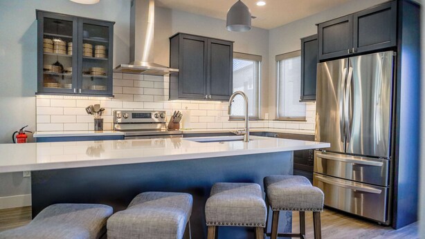 A modern kitchen with dark cabinets, stainless steel appliances, and a central island with bar stools. - The Cornice- Sleeps 8 - AC - Pet Friendly - Modern Townhome (Red Lodge)