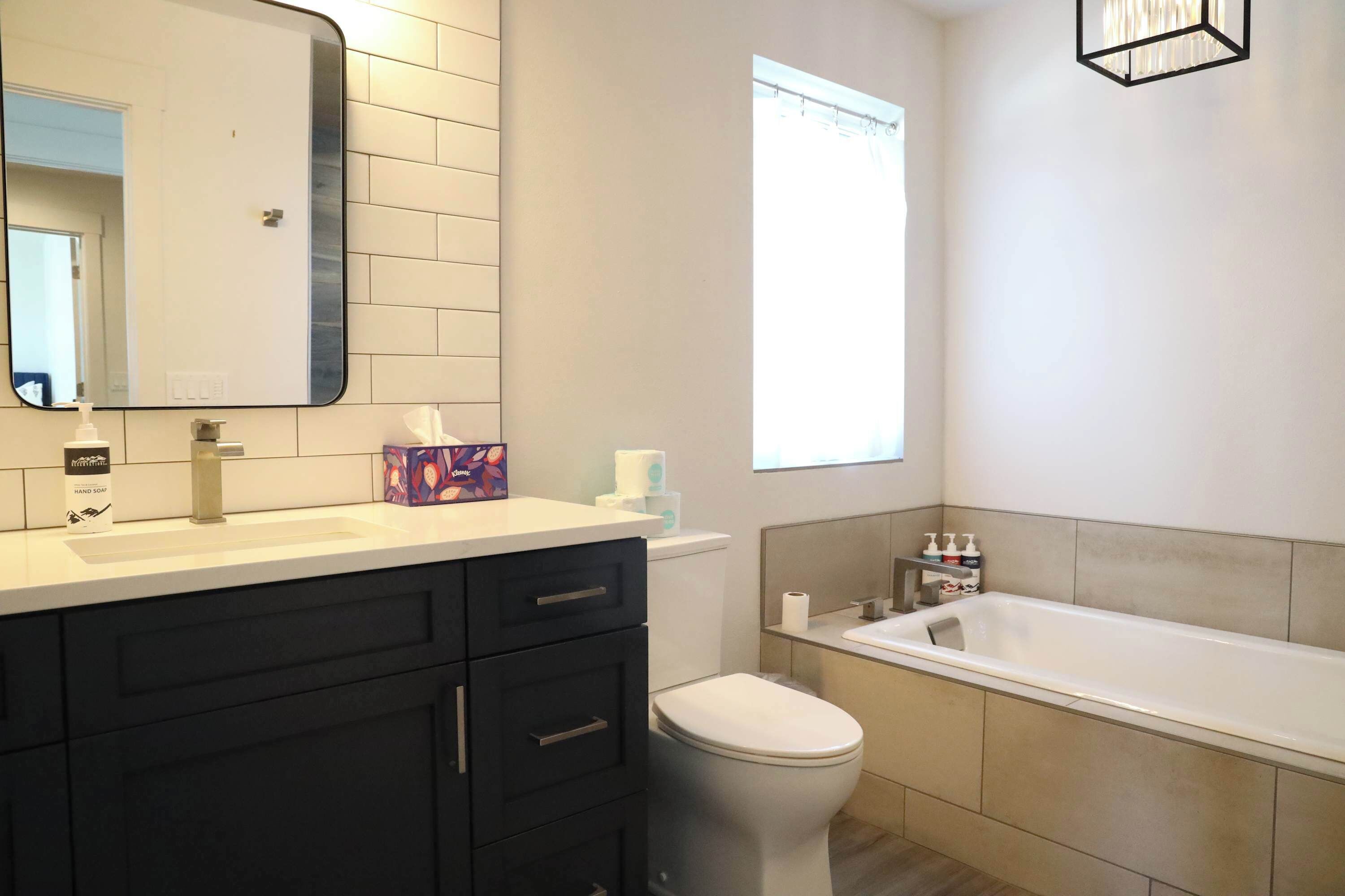 A modern bathroom with a white sink, dark cabinets, a toilet, and a bathtub.