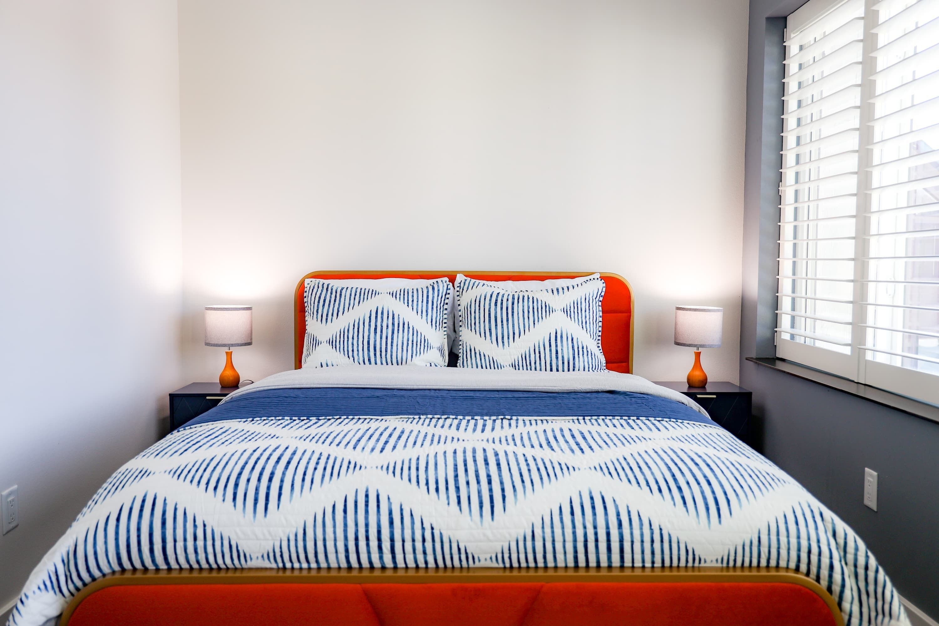 Un letto con una coperta a motivi, due abat-jour e una finestra con persiane.