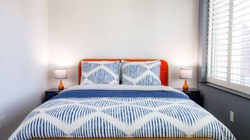 Un letto con una coperta a motivi, due abat-jour e una finestra con persiane.