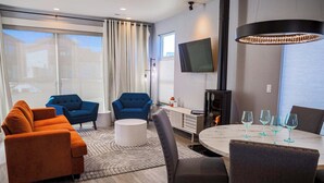 A modern living room with a sofa, chairs, a dining table with glasses, a TV, and a fireplace. - The Cornice- Sleeps 8 - AC - Pet Friendly - Modern Townhome (Red Lodge)