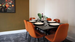 A dining area with a table set for four, featuring orange chairs, white plates, and wine glasses. - Knaresborough Retreat - Group Accommodation (Knaresborough)