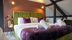A neatly made bed with a green headboard, white and purple bedding, and two white towels on the bed. - Knaresborough Retreat - Group Accommodation (Knaresborough)