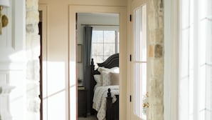 Un arco de piedra que da acceso a un dormitorio con cama, ventana y puerta.
