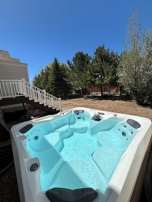 A hot tub with multiple jets, a white deck, and a staircase leading to a house.