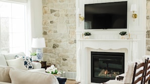 Una sala de estar con pared de piedra, chimenea, televisor y ventilador de techo.