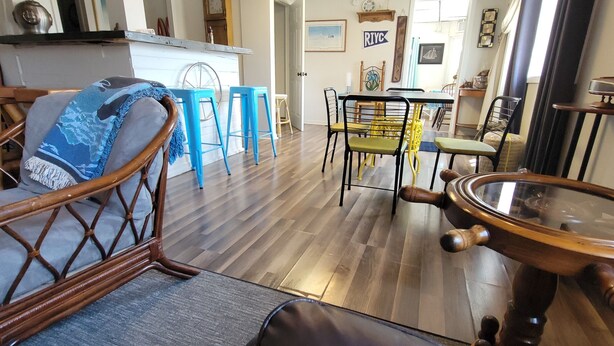 A room with a wooden floor, a dining table with chairs, a wooden stool, and a wooden cabinet with a glass top.
