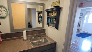 A bathroom with a sink, a mirror, a clock, and a fire extinguisher.