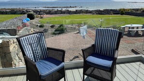 Un patio con sedie in vimini, vista sul mare e un'area verde con piscina.
