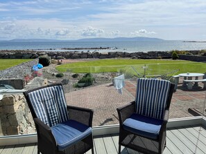 Un patio con sillas de mimbre, vistas al mar y una zona ajardinada con piscina.