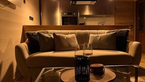 Un salon confortable avec un canapé, une table basse en verre et une cuisine en arrière-plan.