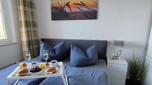 A neatly arranged bedroom with a bed, a bedside table with a lamp, a tray with breakfast items, and a painting on the wall. - Cozy and barrier-free vacation apartment with balcony in Damp. Directly by the sea. (Thumby)
