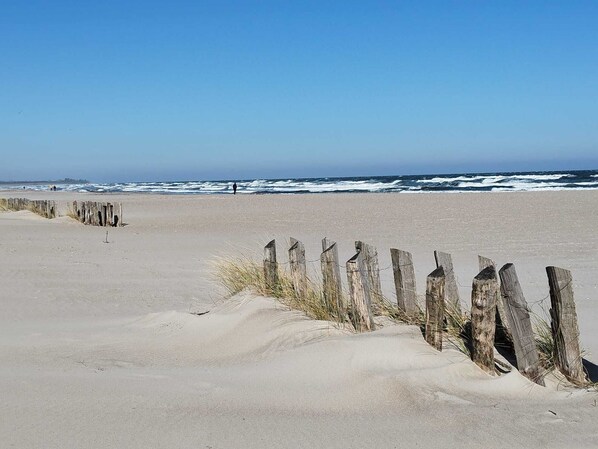Ein Sandstrand mit einer Holzbrüstung und Wellen im Hintergrund.