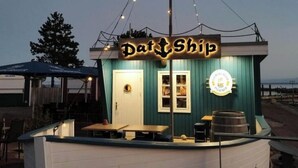 A small, single-story building with a sign reading 'Pat Ship' and a logo on the side. - Cozy and barrier-free vacation apartment with balcony in Damp. Directly by the sea. (Thumby)