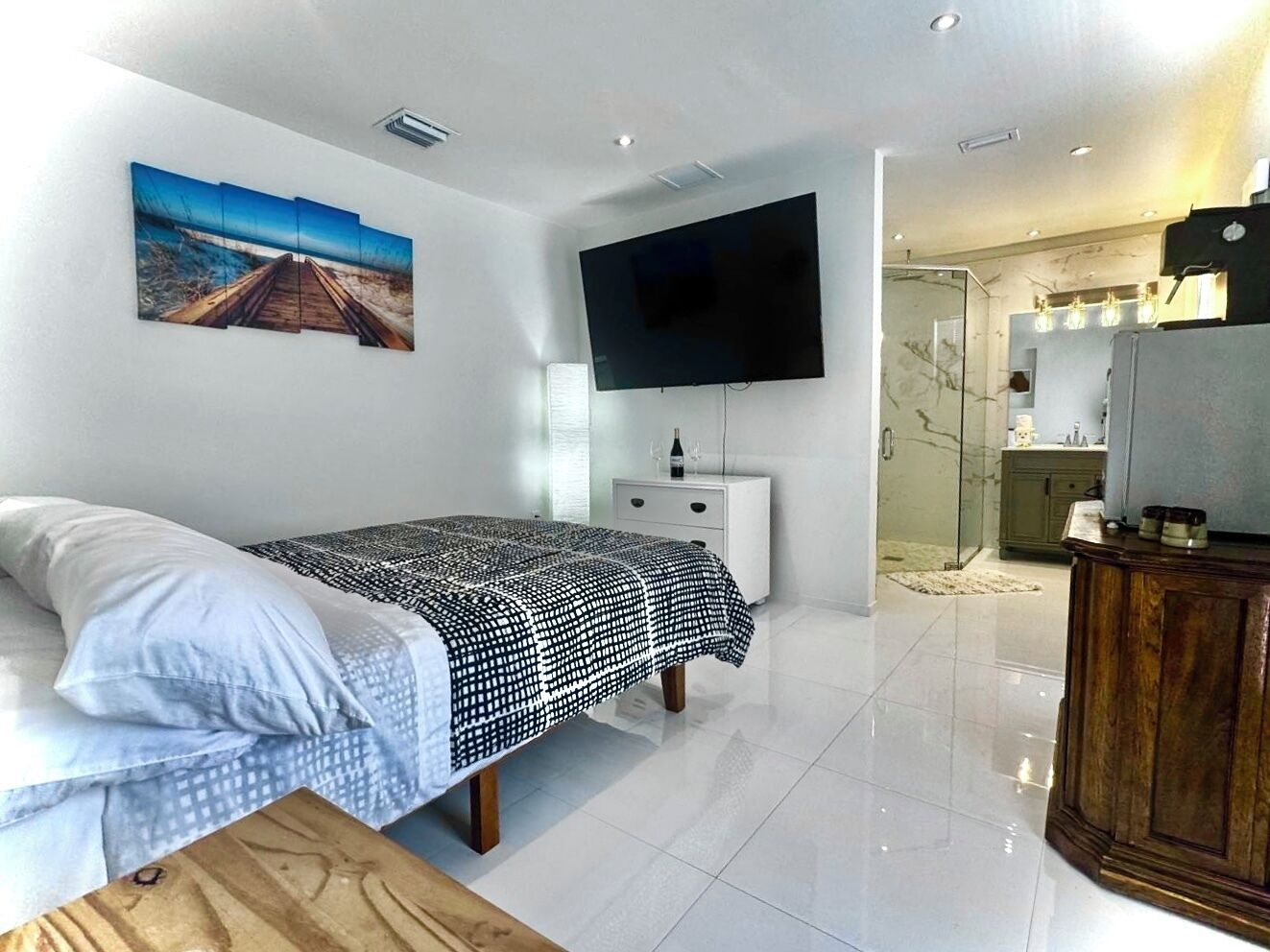 Une chambre d’hôtel moderne équipée d’un lit, d’un téléviseur à écran plat, d’une salle de bain avec une douche en verre et d’une armoire en bois.
