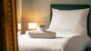 A neatly made bed with a folded towel, a white pillow, and a headboard.