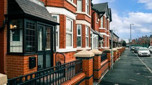 A row of red brick terraced houses with black window frames and white window sills.