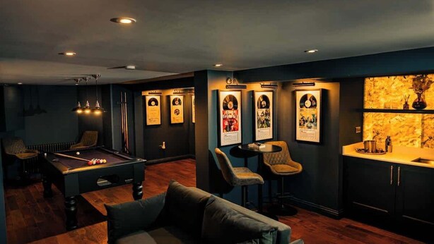 A room with a pool table, a sofa, a bar area with a marble countertop, and framed memorabilia on the walls.