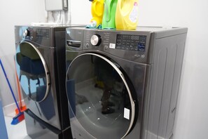 Zwei Waschmaschinen mit Frontlader, Bedienfeldern, einem Spiegel und einer gelben Waschmittelflasche obenauf.