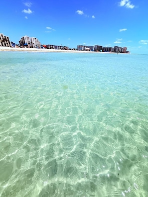 Una playa con aguas cristalinas, edificios al fondo y cielo despejado.