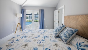 A bedroom with a bed, a lamp, a view of a pool, and a door leading outside.