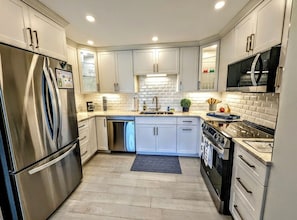 A modern kitchen with stainless steel appliances, white cabinetry, and a tiled backsplash. - Dolphin Watch Waterfront | Indian Shores | Heated Pool | 3-Min Walk to Beach (Indian Shores)