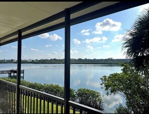 A covered outdoor area with a view of a calm lake, a wooden dock, and surrounding greenery. - Dolphin Watch Waterfront | Indian Shores | Heated Pool | 3-Min Walk to Beach (Indian Shores)