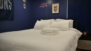 A neatly made bed with white linens and a set of folded towels, a framed picture on the wall, and a neon sign. - Philly Sports Fan Suite Private Entrance + Patio Near PHL (Sharon Hill)
