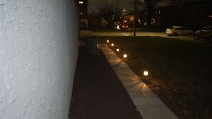 A nighttime street view with a sidewalk, street lamps, parked cars, and a stop sign. - Philly Sports Fan Suite Private Entrance + Patio Near PHL (Sharon Hill)
