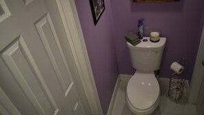 A bathroom with a white toilet, a purple wall, a framed photo, and a toilet paper holder. - Philly Sports Fan Suite Private Entrance + Patio Near PHL (Sharon Hill)