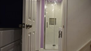 A hallway leading to a bathroom with a glass shower enclosure, a door with a handle, and a step leading to a wooden floor. - Philly Sports Fan Suite Private Entrance + Patio Near PHL (Sharon Hill)