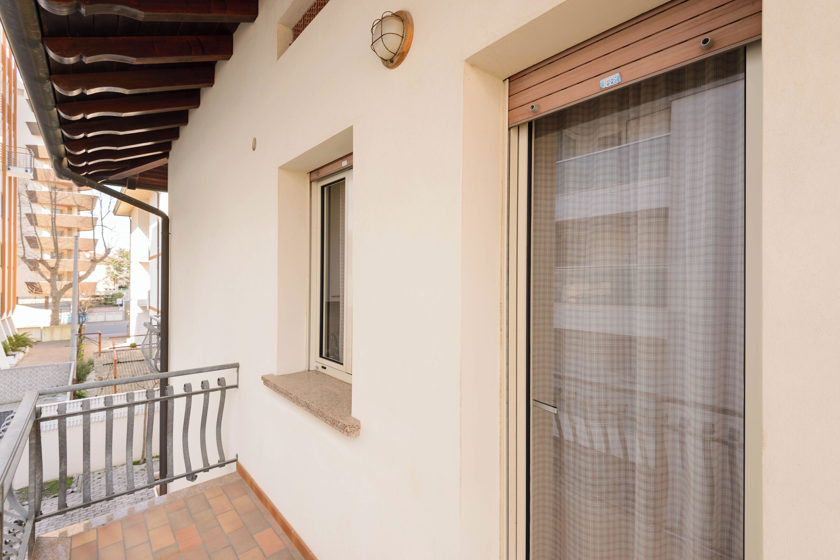 Un balcón con barandilla de metal, una ventana y una puerta con mosquitero.