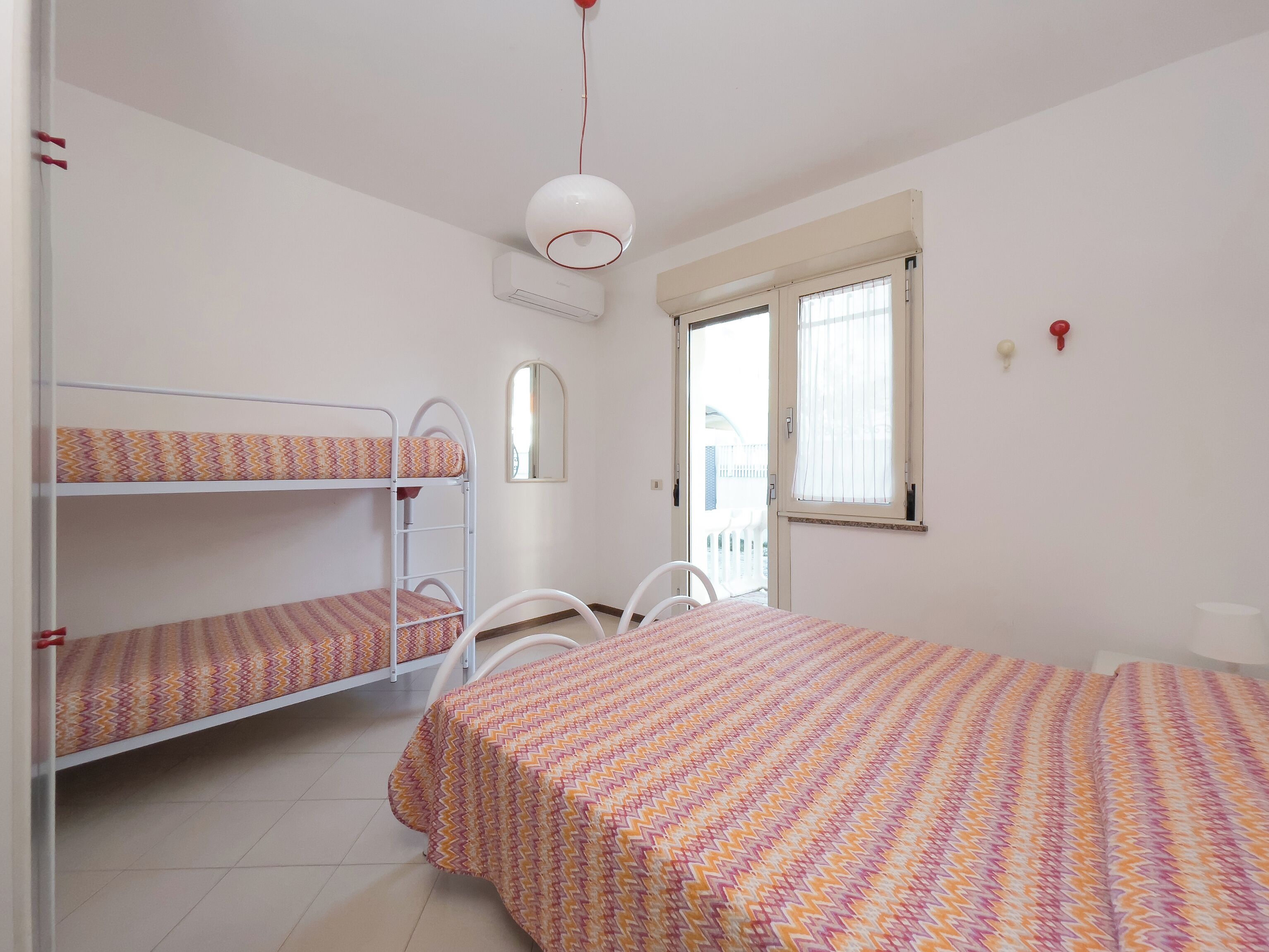 Une chambre avec des lits superposés, un lit simple, un ventilateur de plafond blanc, un appareil de climatisation, une fenêtre avec des rideaux et une porte donnant sur l’extérieur.