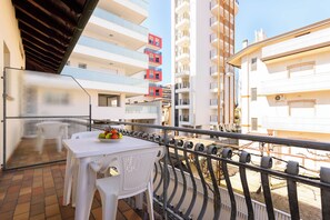 A balcony with a table and chairs, a railing, and a view of adjacent buildings. - Cozy Flat Near Lignano Center (Lignano Sabbiadoro)