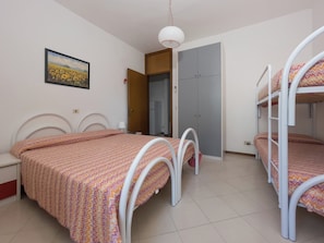 A bedroom with bunk beds, a bedside table, a lamp, a wardrobe, and a painting on the wall. - Comfy Flat Just 350 mt From the Beach (Lignano Sabbiadoro)