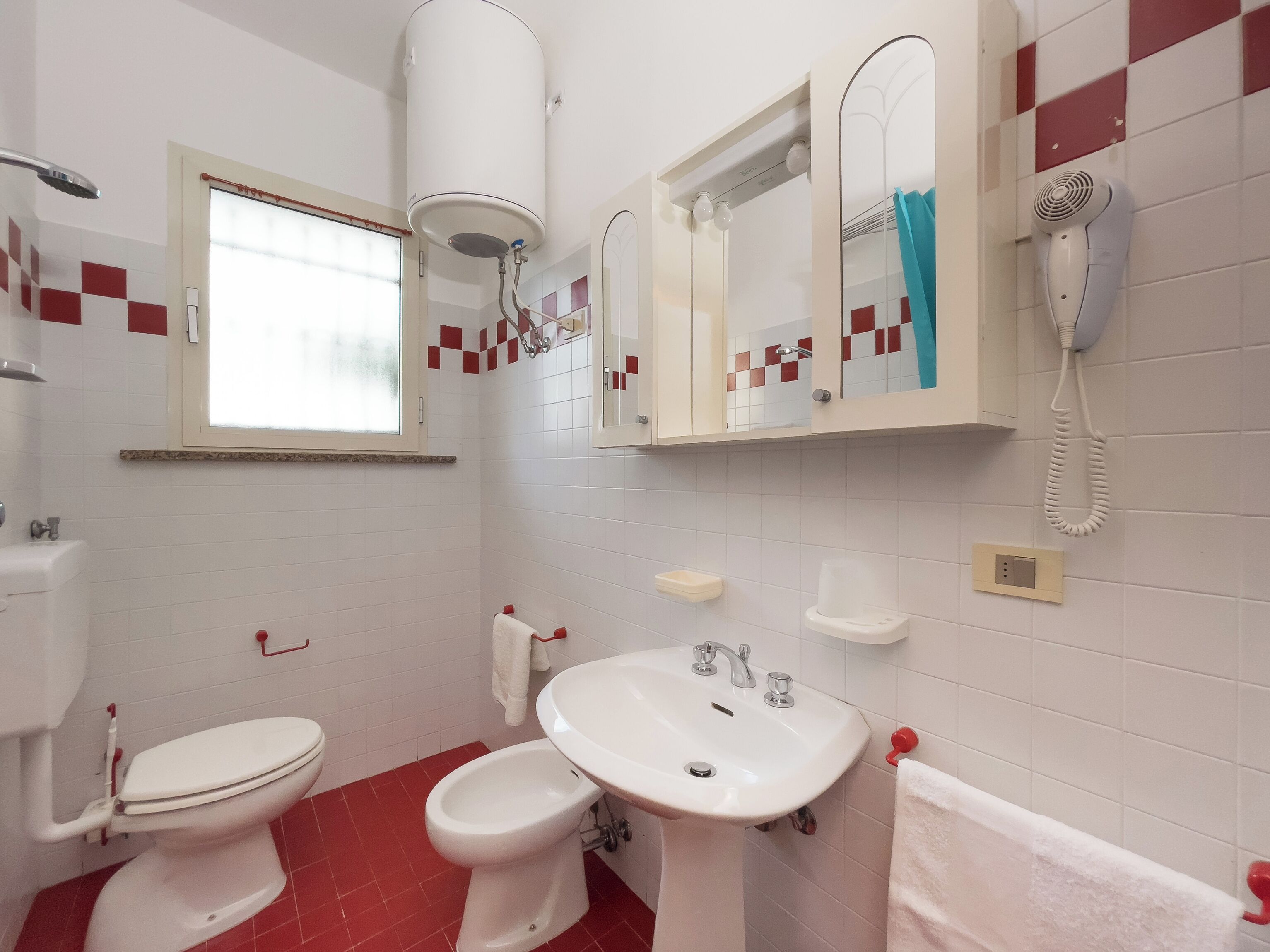A bathroom with a toilet, bidet, sink, mirror, and a hairdryer.