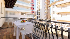 A balcony with a table and chairs, a railing, and a view of adjacent buildings. - Lignano Sabbiadoro Flat With Terrace (Lignano Sabbiadoro)