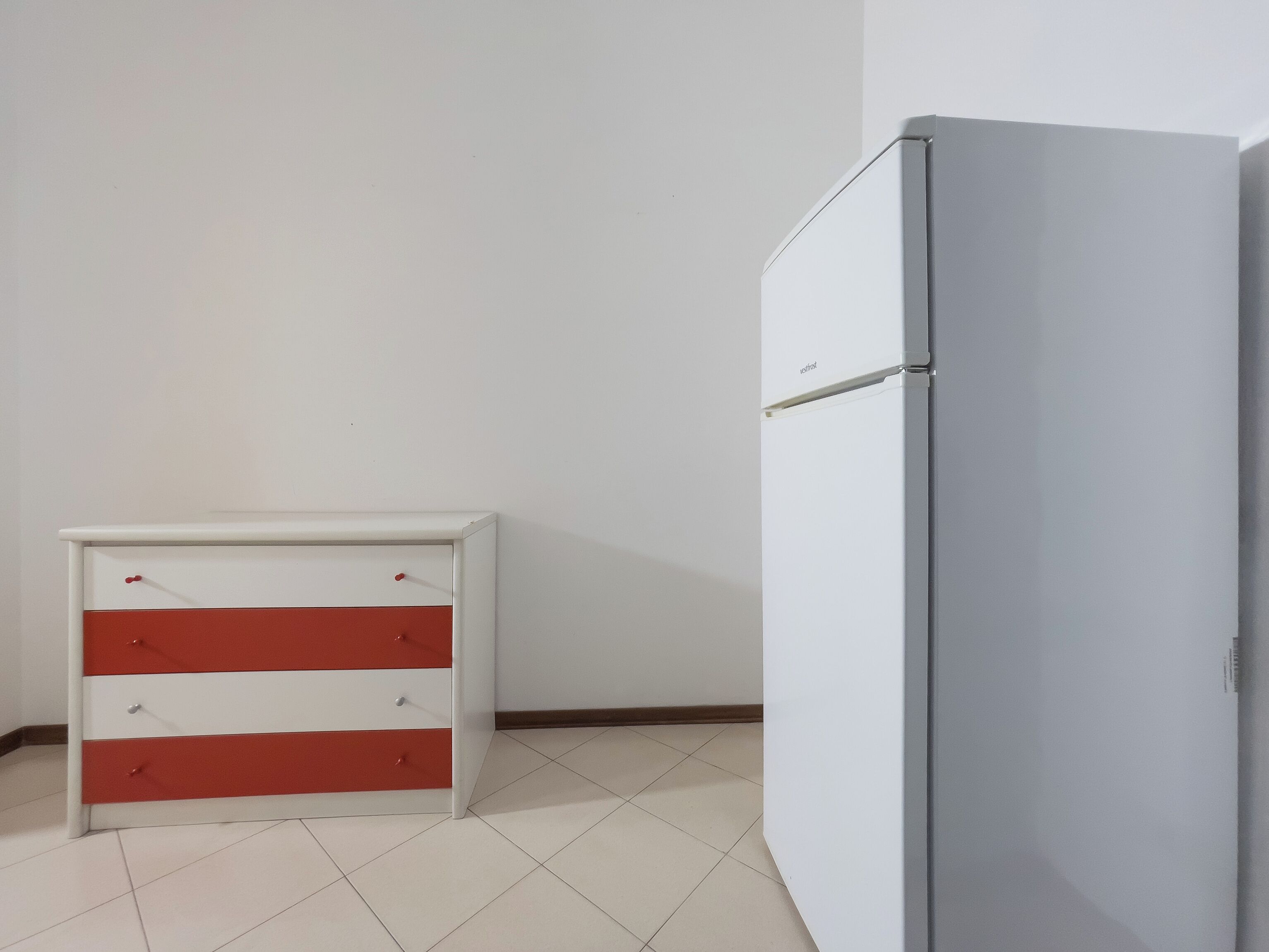 Ein Zimmer mit einem weißen Schrank, der rote Schubladen und einem weißen Kühlschrank hat.