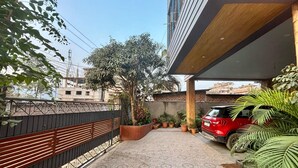 A paved patio with a tiled floor, a red car parked, and potted plants.
