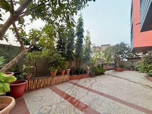 Un patio con plantas en macetas, piso de baldosas y un edificio al fondo.