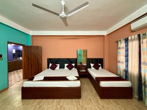 Una habitación de hotel con dos camas, un ventilador de techo, un espejo y un baño visible a través de una puerta abierta.