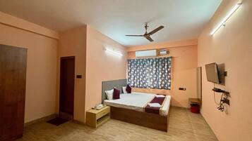 A bedroom with a bed, a ceiling fan, an air conditioning unit, a television, and a wooden floor.