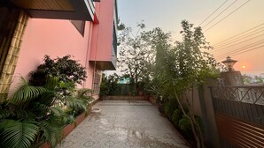 A narrow pathway leading to a building with a pink facade, surrounded by greenery and a traditional lamp post.
