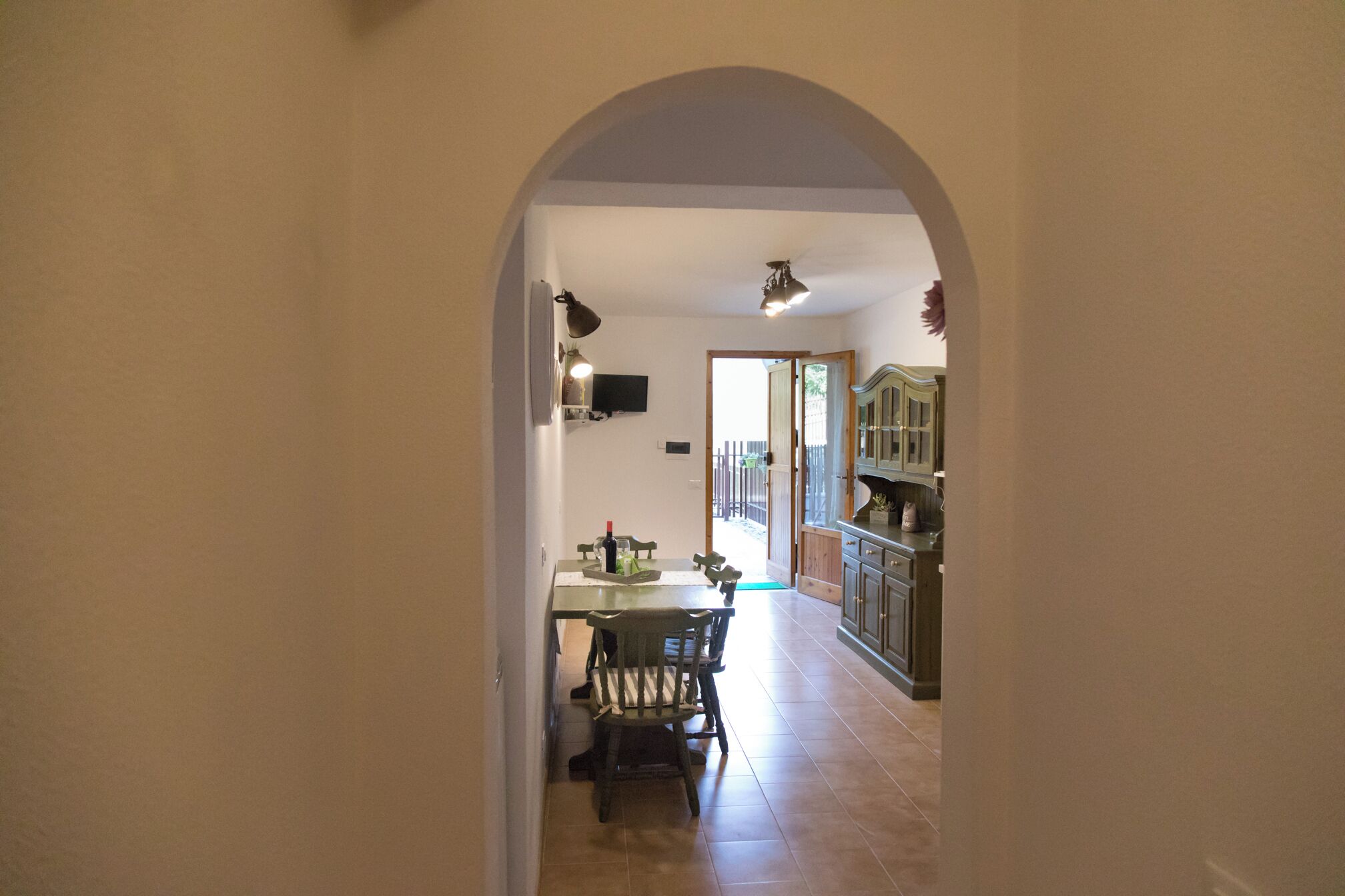 Eine gewölbte Diele führt zu einem Essbereich mit Tisch und Stühlen, einem Deckenventilator und Blick in eine Küchenzeile mit Schränken und einem Fenster.