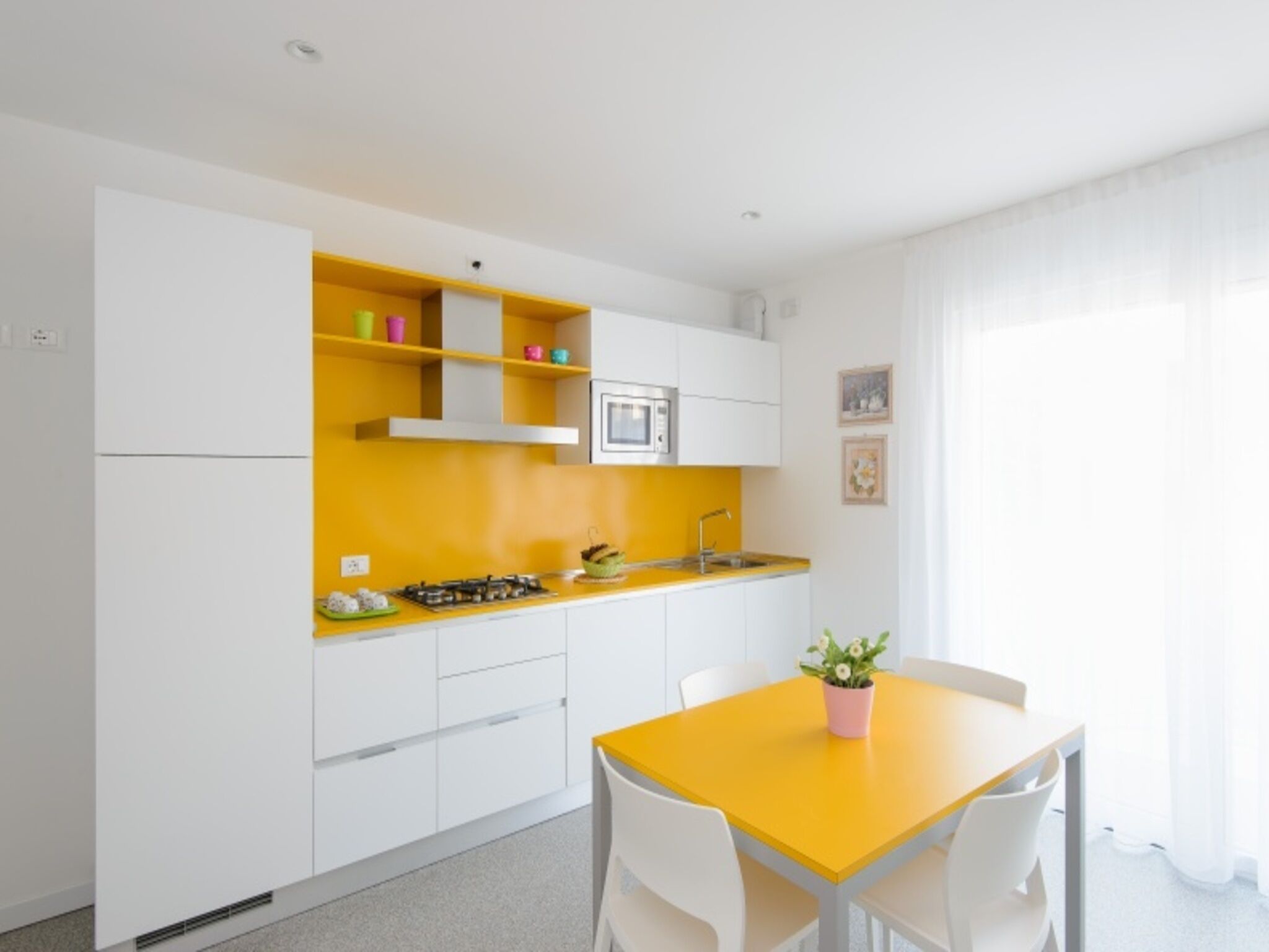 Una cucina compatta con mobili bianchi, un piano di lavoro giallo, un fornello a gas, un forno a microonde e un tavolo con sedie.