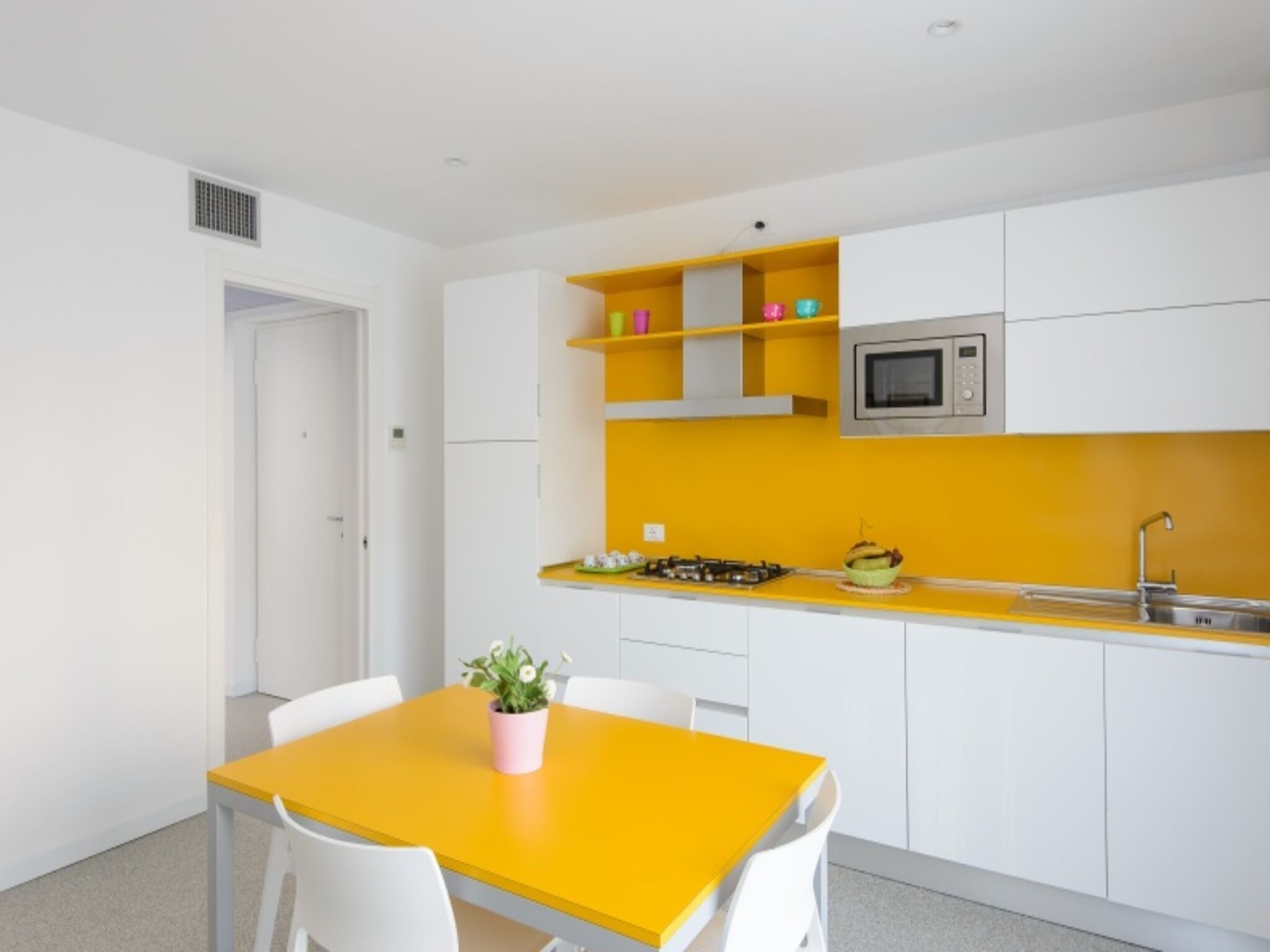 A modern kitchen with white cabinets, a yellow countertop, a microwave, and a sink.