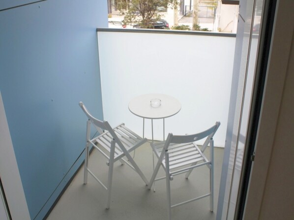 A balcony with a white table and two white chairs, a blue wall, and a view of the street. - Colorful Property in Lignano (Lignano Sabbiadoro)