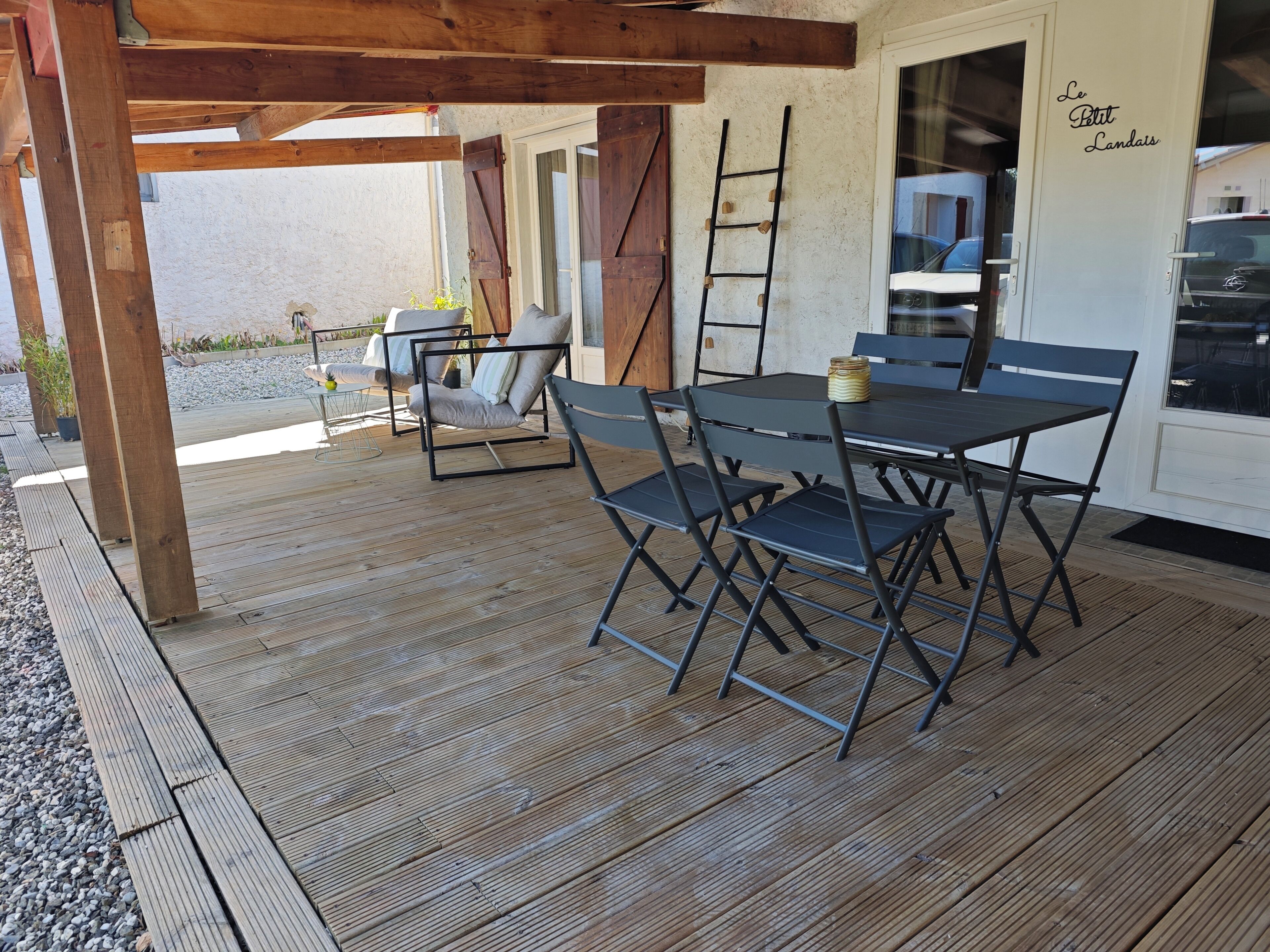 A covered outdoor seating area with a table and chairs, a ladder, and a door with signage.