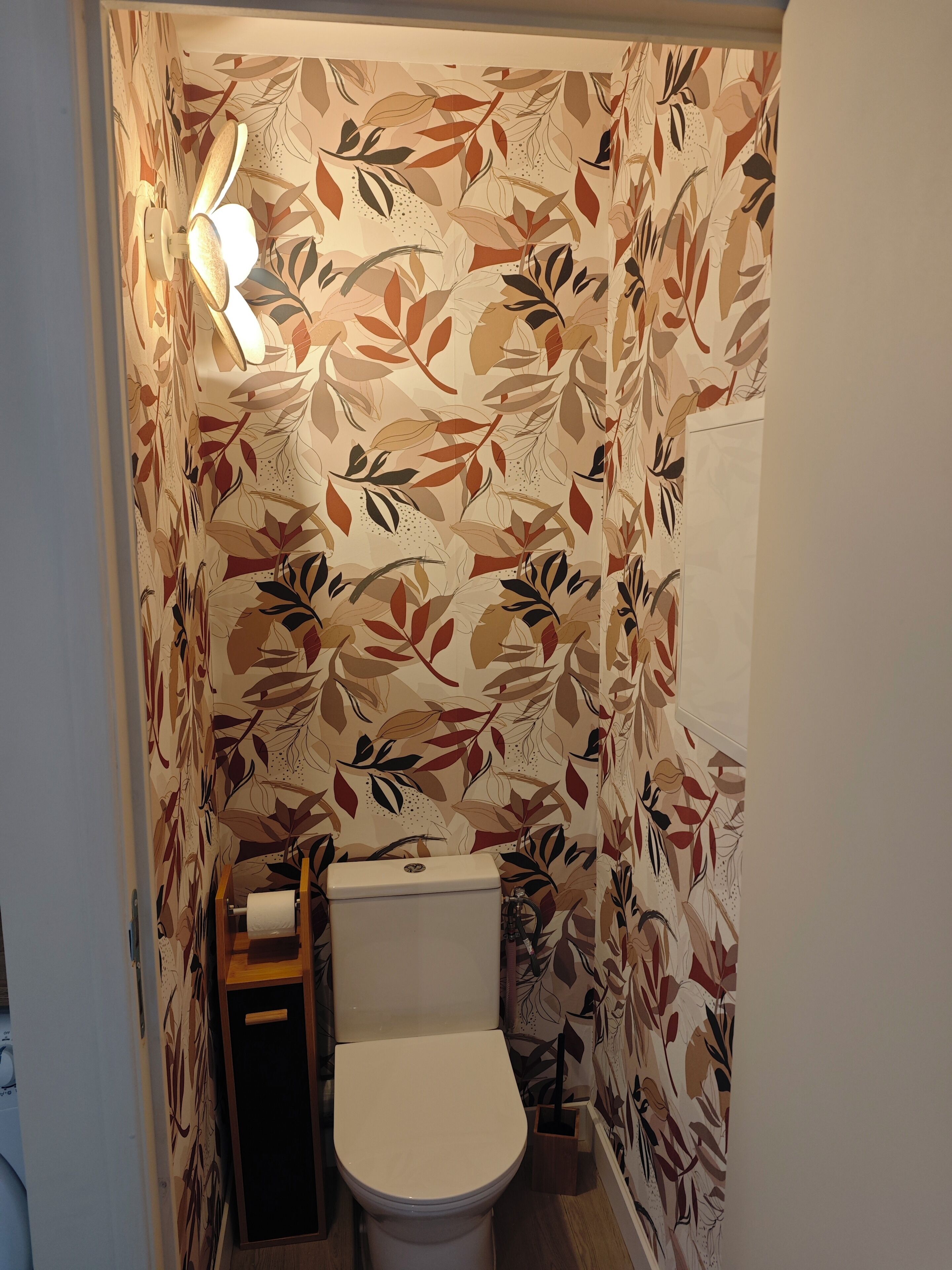 Een badkamer met een toilet, een rol toiletpapier en een wandlamp.