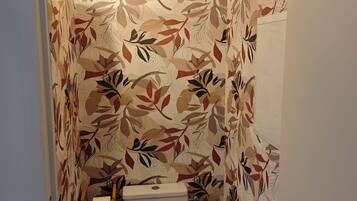 Een badkamer met een toilet, een rol toiletpapier en een wandlamp.